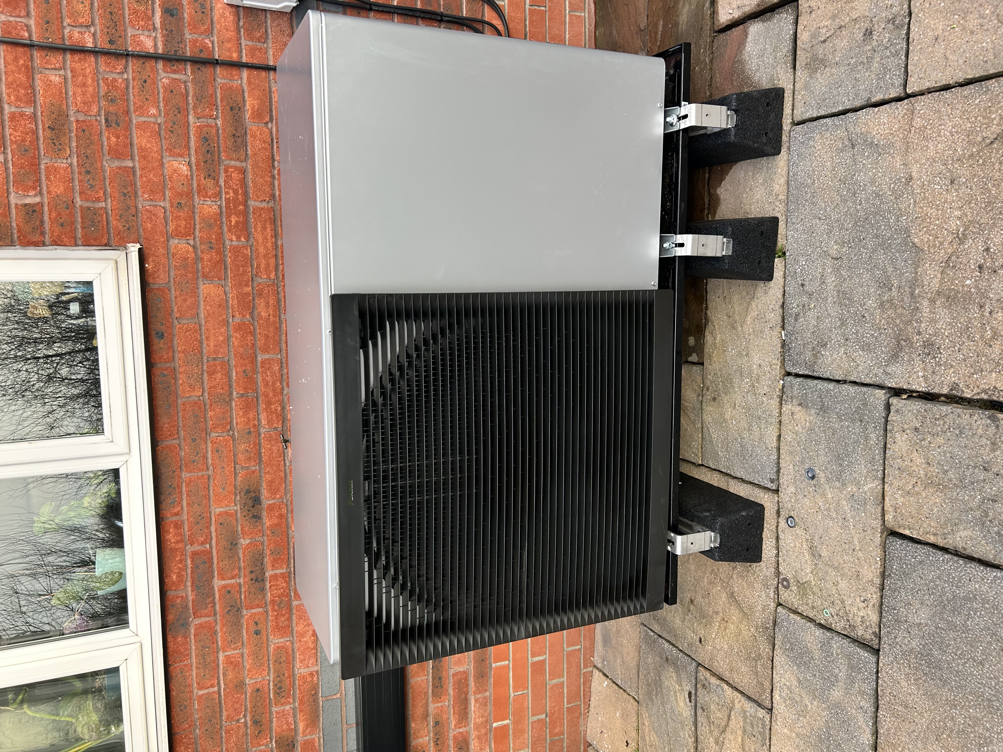 Modern air source heat pump installed on anti-vibration feet outside a home