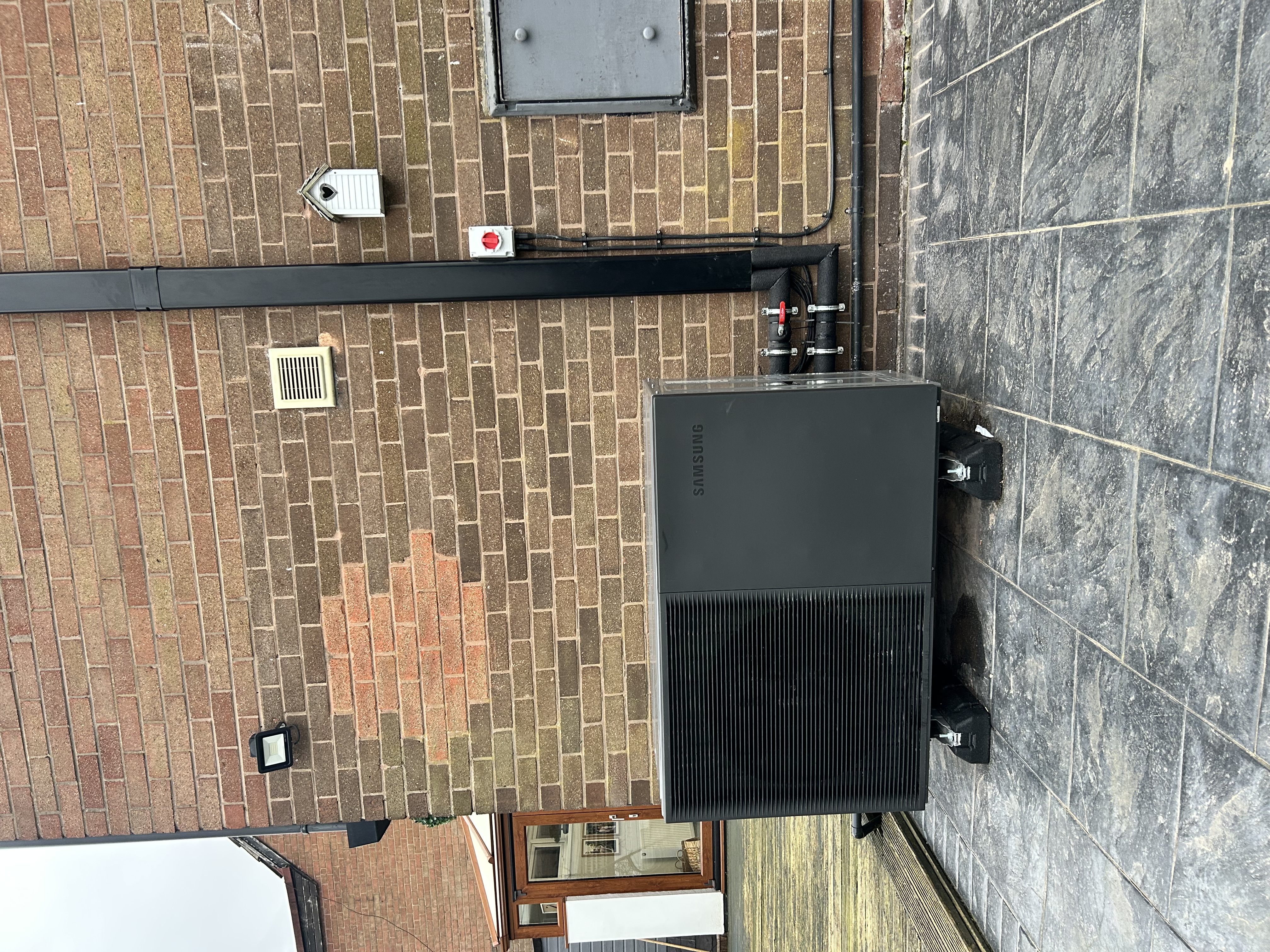 Samsung air source heat pump installed beside a brick home